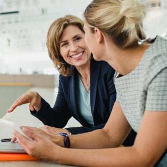 An HR professional sitting down with an employee smiling and talking.